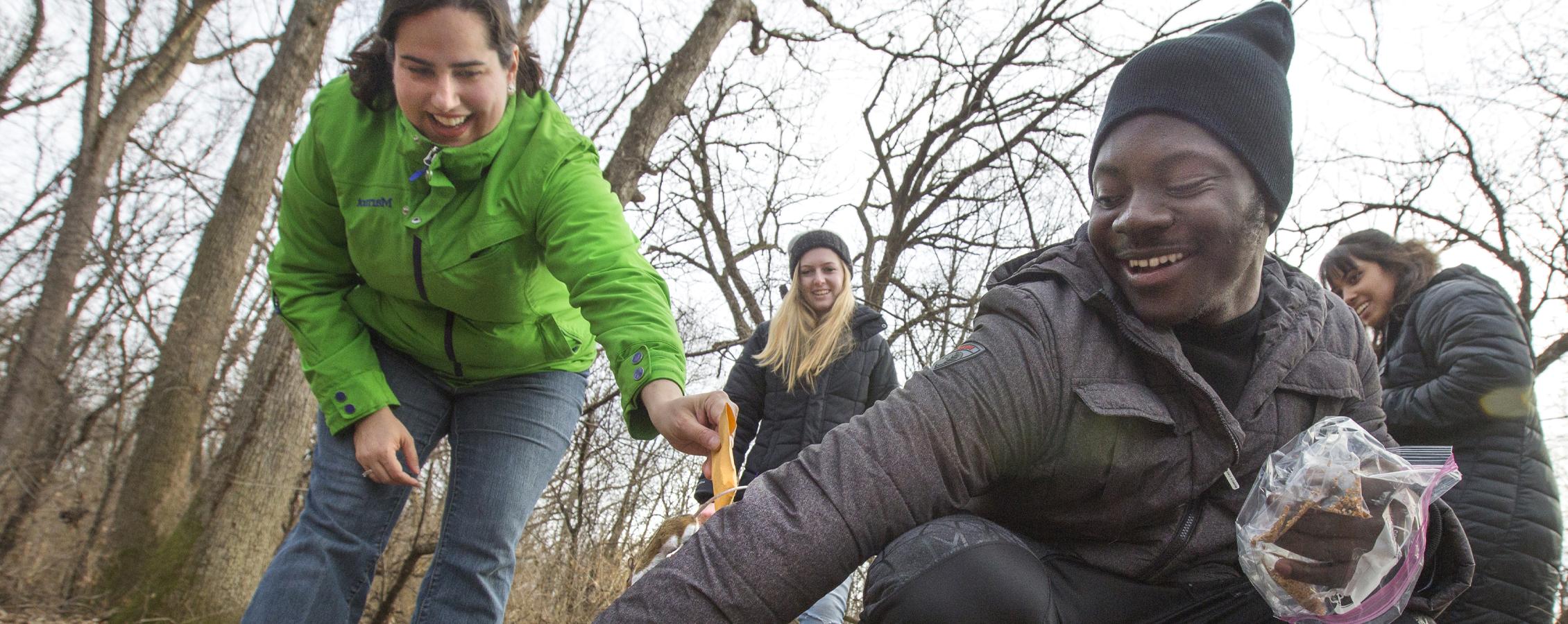 A student holds out their arm as a mouse runs up while they're in the woods for class.