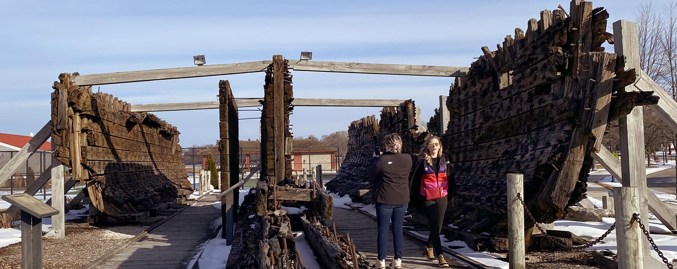 Students walk through remains of an old, large wooden boat.