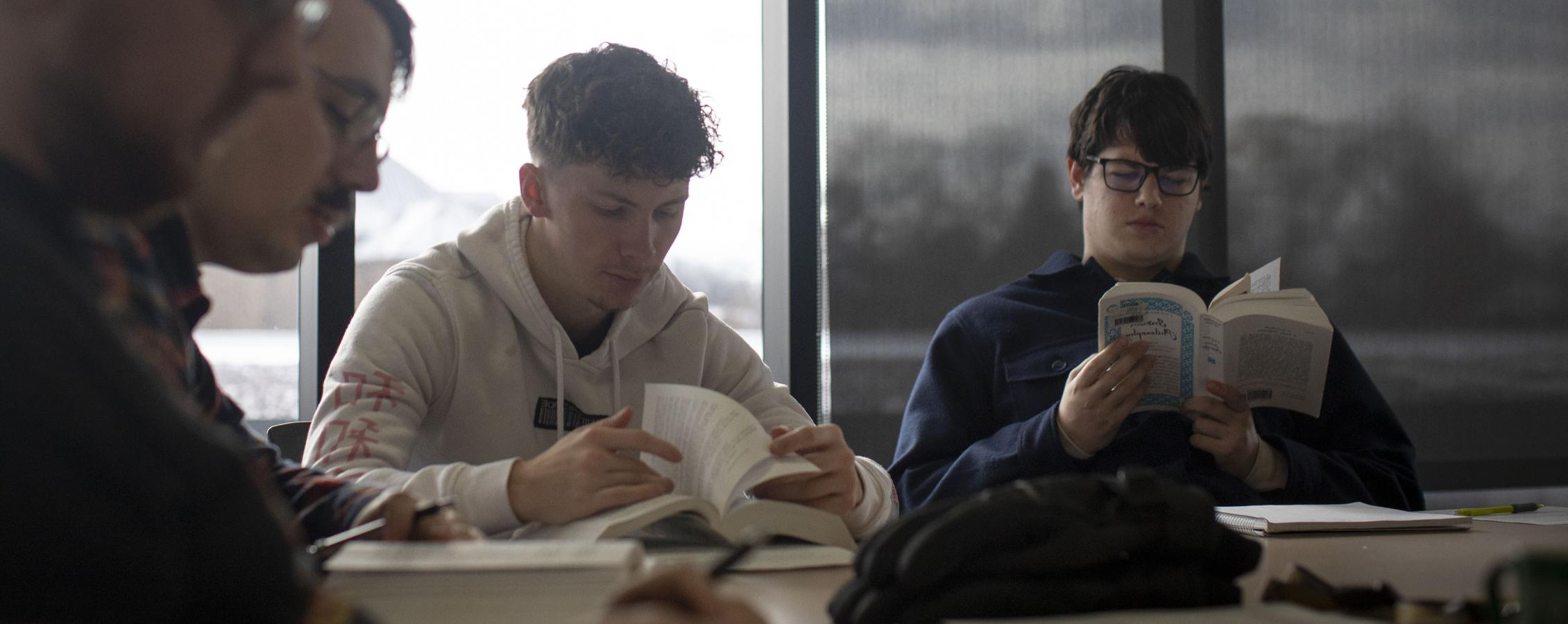 Students gather around a table reading books.