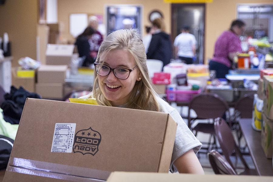 A student smiles while carrying a cardboard box.