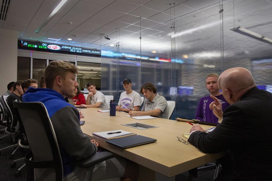 Students and a faculty member sit around a table with computer monitors in the background.