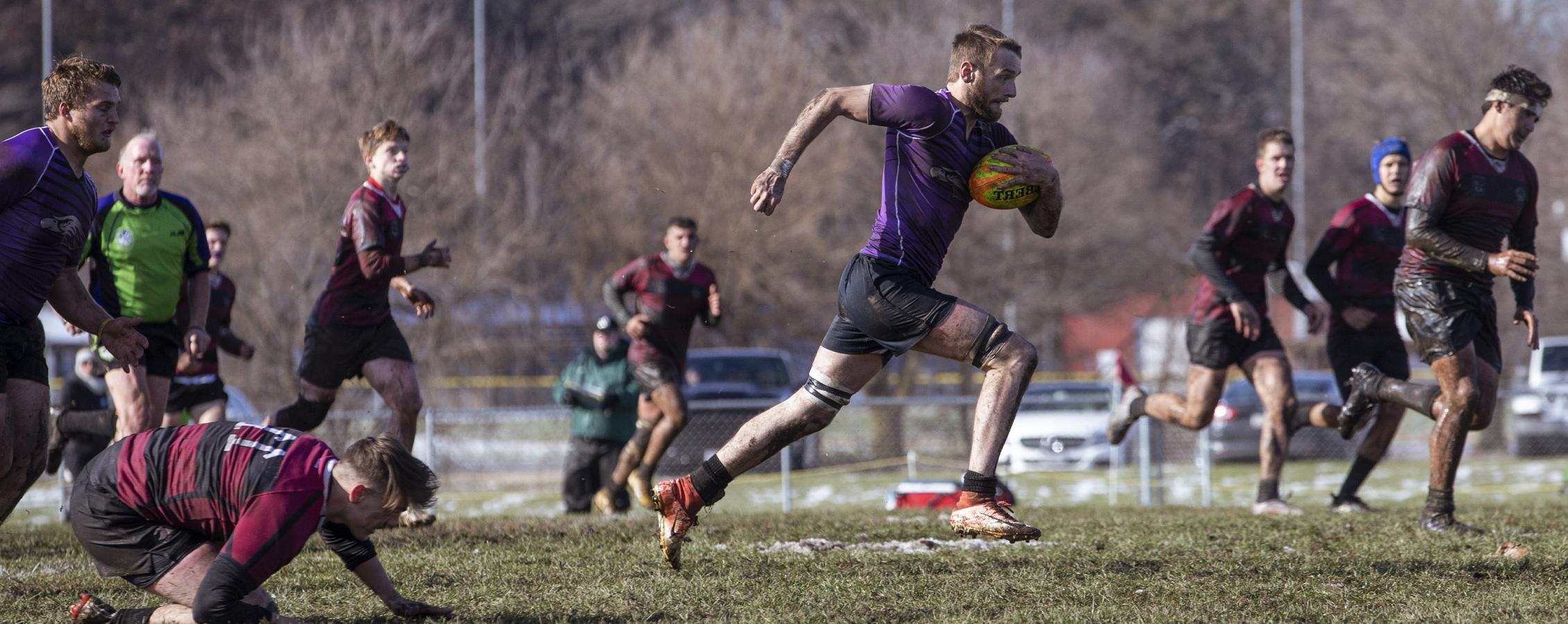 A Warhawk men's rugby player runs with the ball.