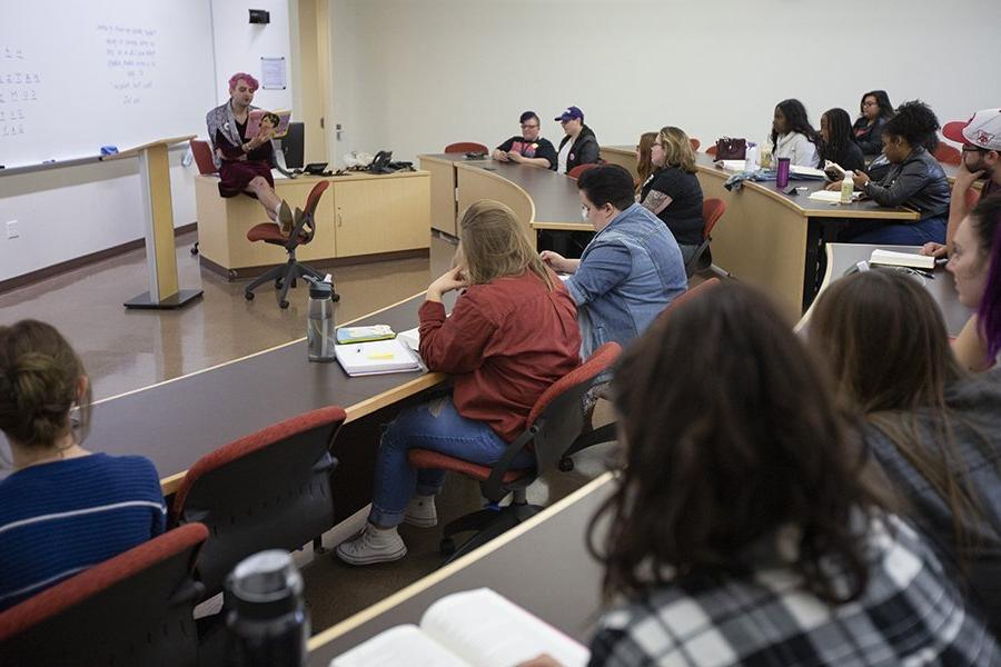 Jacob Tobias, a guest speaker, reads from a book at the front of a class.