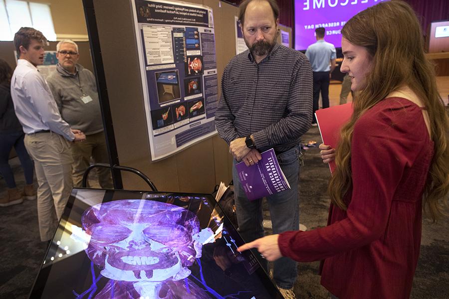 A student shows work to a faculty member on a virtual image of the muscular system of a human head and neck.