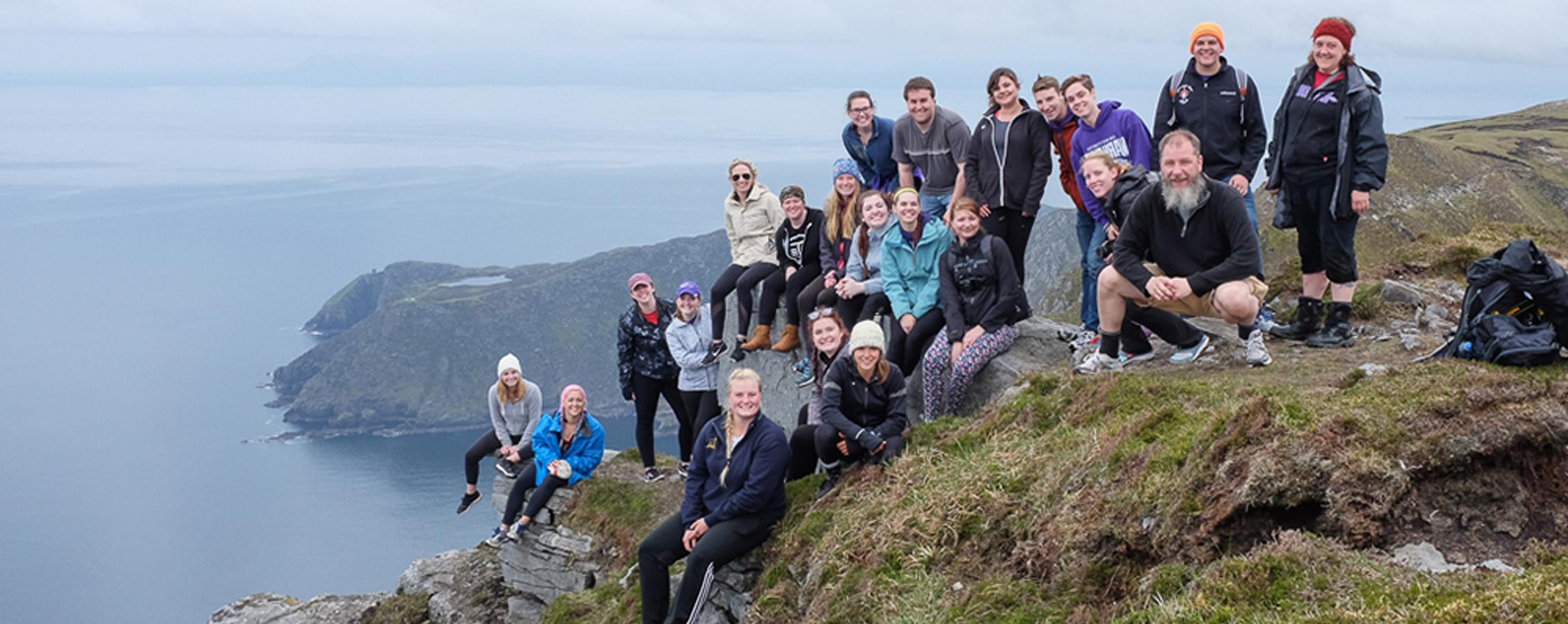 Students and a faculty member sit along the edge of a cliff overlooking the sea.