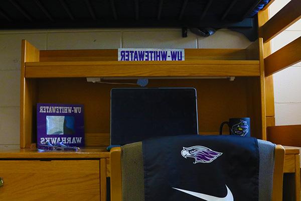 Underneath a lofted bed, there is a desk with a laptop on top of it.