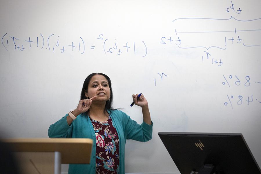 Rashiqa Kamal smiles stands in front of a white board with mathematical equations.