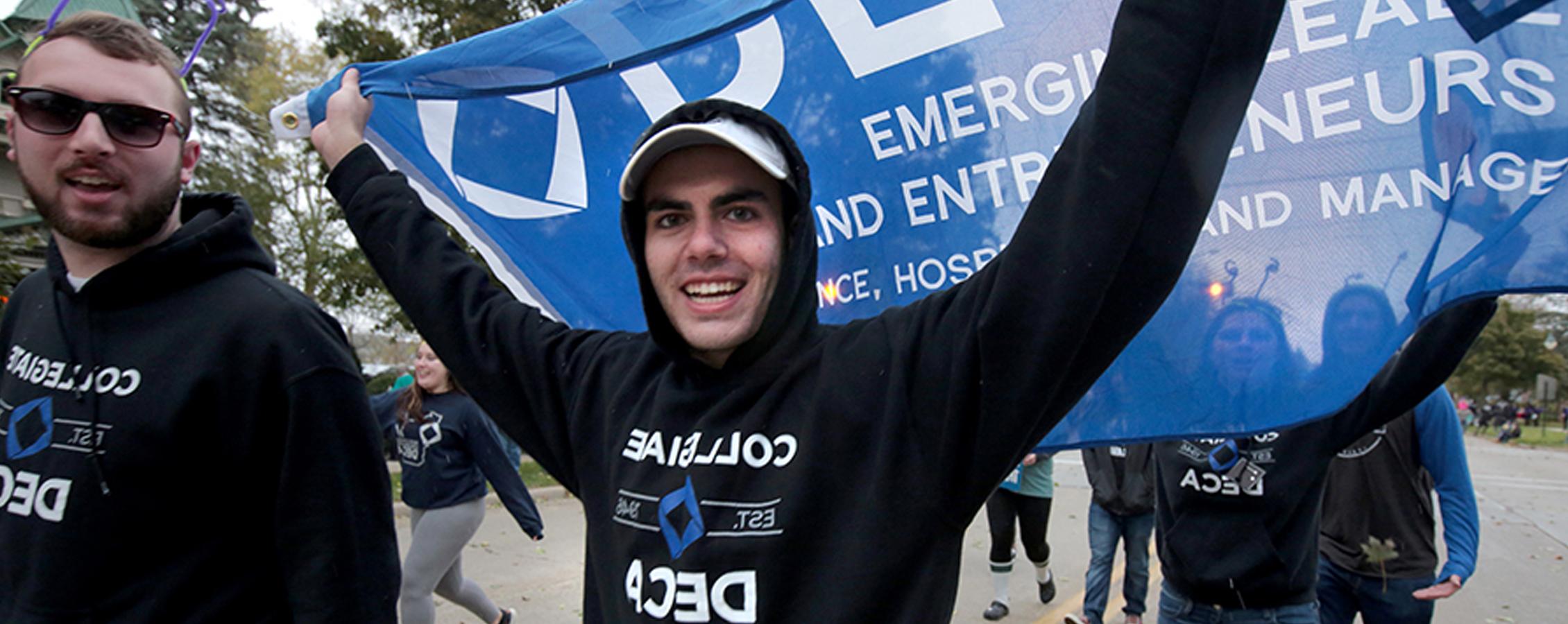 A student holds a blue DECA flag behind him while marching in the Homecoming parade.