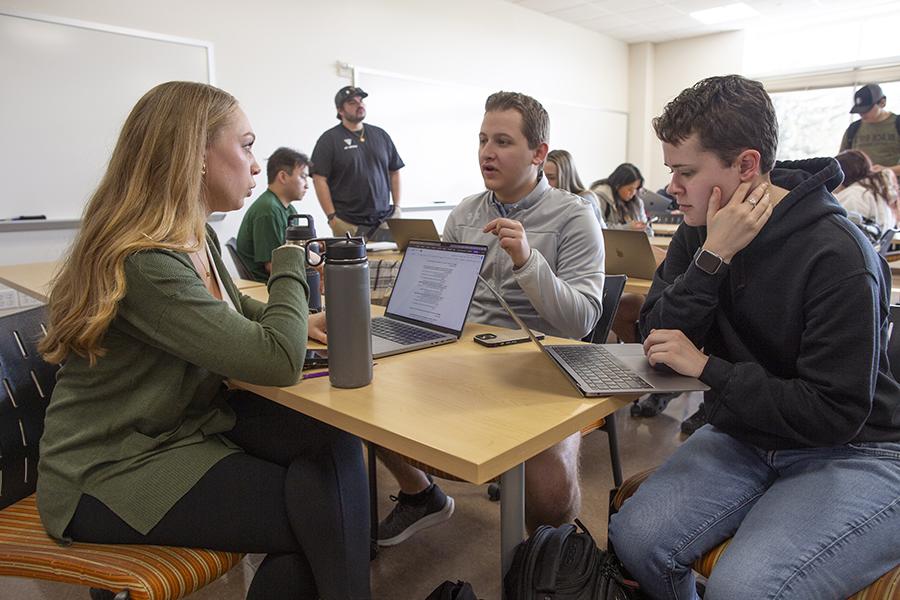 Students smile and laugh together in a classroom with bright windows in the back of the room.